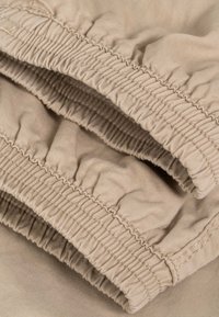 Primer plano de tela beige con puños elásticos y costuras detalladas en mangas de ropa o piernas de pantalón.