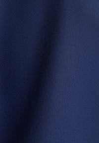 Dunkelblauer Stoff mit subtiler Textur und weichen Falten, die Schatten- und Lichtvariationen auf der Oberfläche erzeugen.