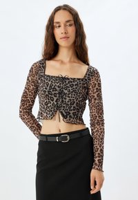 Leopardenmuster cropped Top mit langen durchsichtigen Ärmeln, quadratischem Ausschnitt und Kordelzug-Detail vorne; kombiniert mit einem schwarzen Bleistiftrock und einem Gürtel.