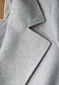 Jasnoszary wełniany płaszcz z wykładanym kołnierzem i starannymi detalami szwów. Materiał ma miękką, teksturowaną powierzchnię.