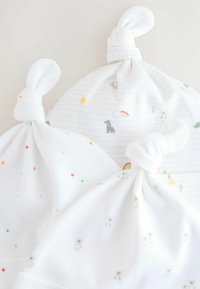 Trois couvertures pour bébés en coton blanc nouées, arborant des motifs d'étoiles colorées et des illustrations d'animaux, dont un zèbre, un ours et un arc-en-ciel.