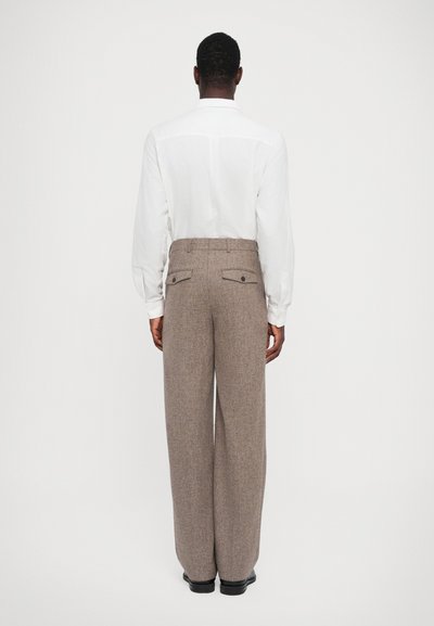 Pantalons marron taille haute avec une finition texturée, dotés de deux poches arrière et d'une jambe large. Associés à une chemise blanche à manches longues.