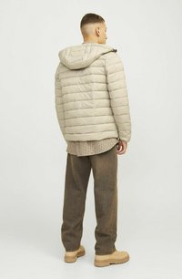 Doudoune beige avec motif matelassé horizontal, capuche attachée et fermeture éclair à l'avant. Portée sur une chemise à carreaux et associée à un pantalon marron.