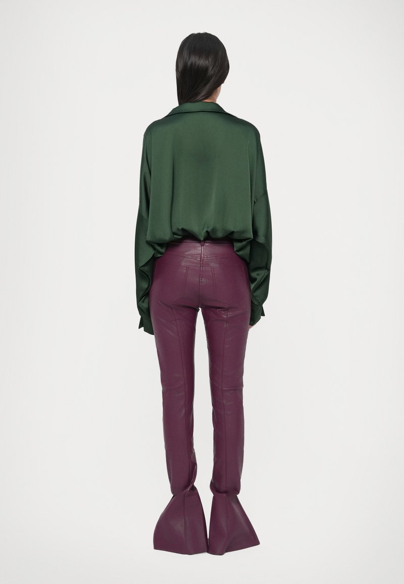 Satin green oversized shirt with a collar paired with fitted, pu purple pants featuring flared hems. Smooth texture and modern design details.