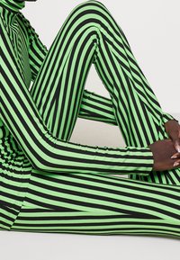 Zielono-czarny body w paski z długimi rękawami, o dopasowanym kroju i gładkiej fakturze. Paski mają naprzemienną szerokość.