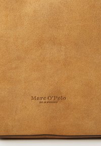 Borsa in suede color tan con texture liscia e logo "Marc O'Polo" in rilievo, dal design minimalista e linee pulite.