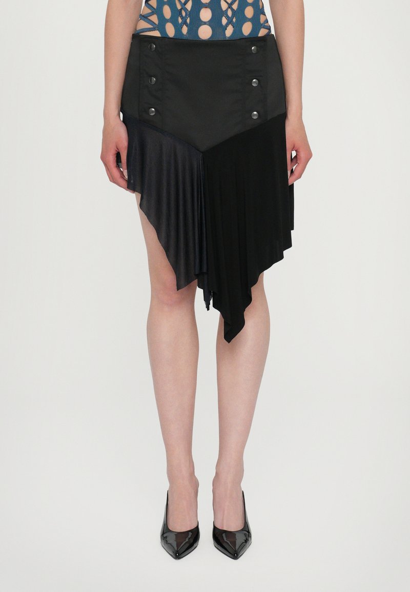 Jupe asymétrique noire avec un mélange de textures mates et plissées, ornée de détails en boutons à la taille et d'un ourlet en dents de scie.
