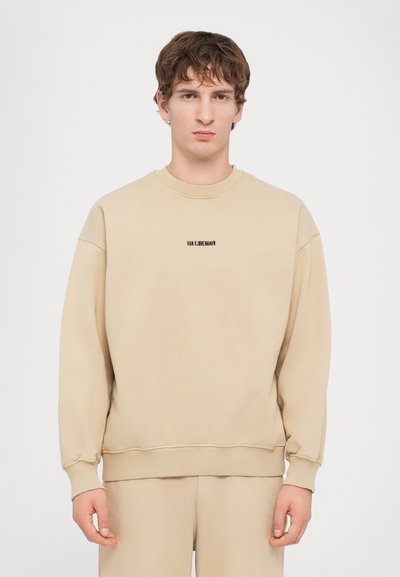 Beige sweatshirt med lange ærmer, rund halsudskæring, ribbede manchetter og kant. Centreret tekstlabel i sort: "HAN X LÄBEBEWARN." Glat tekstur.