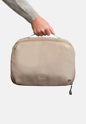 Custodia per laptop in tessuto beige con texture liscia, manico robusto e chiusura con zip. Presenta un piccolo logo sul davanti.