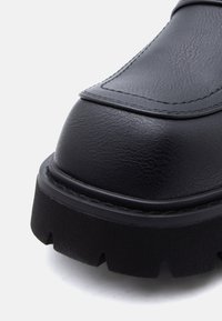 Μαύρο δερμάτινο παπούτσι με στρογγυλεμένη μύτη, υφή στην επιφάνε ια και παχιά, ανθεκτική σόλα με βαθιές αυλακώσεις και ματ φινίρισμα.