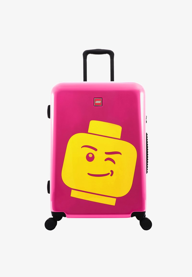 Růžový tvrdý kufr s designem žluté LEGO postavy, se teleskopickou rukojetí, čtyřmi černými kolečky a logem LEGO.