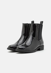 Bottes de cheville en cuir verni noir avec des côtés élastiques, semelle plate, bout pointu et clous décoratifs sur les côtés. Fini lisse et brillant.