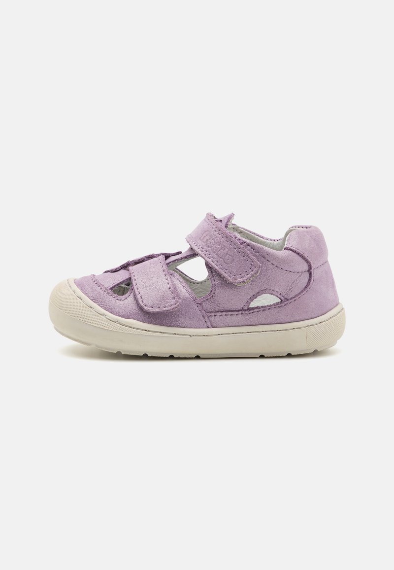 Lila mockaskandaler med två justerbara kardborreband, utdragna detaljer på sidorna och en vit gummisula. Har en rundad tån design.
