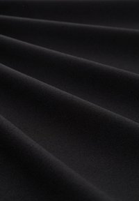 Tessuto nero con una texture liscia, caratterizzato da profonde pieghe che creano un motivo a onde. Il materiale appare morbido e leggermente opaco.