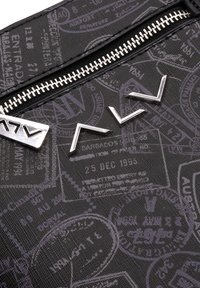 Tessuto nero texturizzato con timbri da viaggio in rilievo, zip argentata e accenti metallici in un design geometrico.
