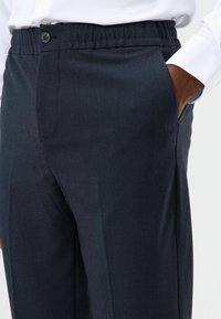 Dunkelblaue Hose aus strukturiertem Stoff, mit elastischem Bund, Knopfverschluss und Seitentaschen.