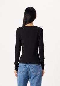 Μαύρη μακρυμάνικη μπλούζα με ριγωτή υφή και στρογγυλή λαιμόκοψη, συνδυασμένη με ανοιχτό μπλε ψηλόμεσα τζιν που διαθέτουν κλασι κές πίσω τσέπες.