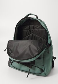 Groene stoffen rugzak met een zwarte binnenkant. Beschikt over een ritssluiting, een gewatteerd vak en een luchtige zijzak. Textuur aan de buitenkant.