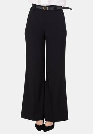 Pantaloni neri a gamba larga abbinati a una cintura nera con fibbia rotonda dorata e décolleté nere con punta appuntita.