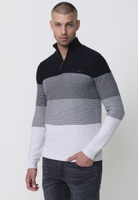 Pullover-Sweater mit einem gestreiften Design in Schwarz und Grau, der einen Reißverschlusskragen, gerippte Bündchen und einen einfarbigen weißen unteren Abschnitt hat.
