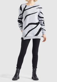 Felpa grigia chiara con design astratto a strisce nere, maniche lunghe, scollatura rotonda e vestibilità comoda, abbinata a jeans skinny neri e stivali da combattimento.