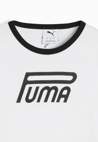 Biela tričko s čiernym golierom, s výrazným čiernym logom "PUMA" vytlačeným na prednej strane. Štítok viditeľný vo vnútri goliera.