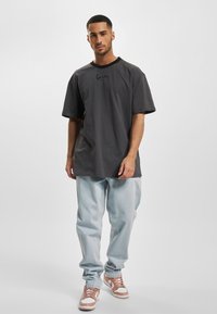 Gray oversized t-shirt with black neckline, featuring an embroidered logo. Paired with light blue jeans and brown sneakers.