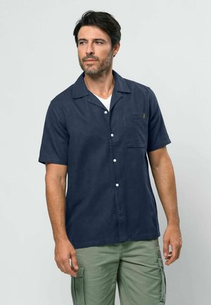 Krátký rukáv námořnicky modré košile z lehké látky, s zapínáním na knoflíky vpředu, levou kapsou na hrudi a volným límcem.