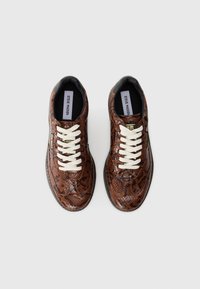 Brune sneakers med slange-mønster, hvide snørebånd, rund tå og tekstureret overflade. Brandlabel synlig på siden og hælen.