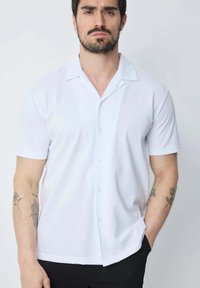 Chemise blanche à manches courtes avec un col camp, en tissu lisse, offrant une coupe décontractée et un ourlet droit.