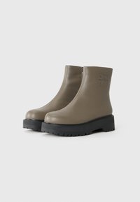 Botine din piele taupe cu talpă groasă neagră și fermoar lateral, embosate cu logo-ul DKNY pe glezna exterioară.
