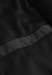 Tessuto nero con una striscia liscia e lucida dal leggero riflesso, contrastata da un pannello testurizzato e soffice per un maggiore effetto di profondità.