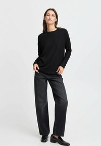 Maglietta nera a costine con maniche lunghe abbinata a jeans in denim scuro a vita alta. L'outfit presenta un taglio dritto e scarpe nere lucide.