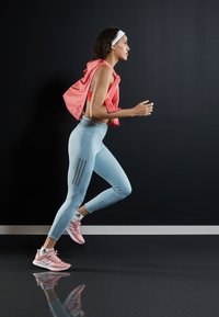Athlète portant un débardeur rose et des leggings bleu clair avec trois bandes grises, chaussée de chaussures de course roses, dans une pose de course dynamique.