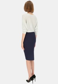 Jasnoszary sweter z bufiastymi rękawami, zestawiony z granatową spódnicą ołówkową i czarnymi szpilkami, widok z tyłu.