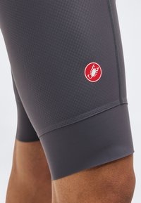 Κοντινή λήψη γκρι σορτς ποδηλασίας με υφασμάτινη υφή και κόκκινο κυκλικό λογότυπο με άσπρο σκορπιό στο μηρό ενός ατόμου.