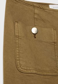 Gros plan d'une poche de pantalon en tissu beige avec une fermeture à bouton-pression en métal et des détails de couture visibles.