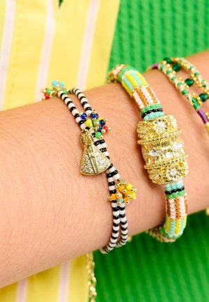 Trois bracelets : un avec des rayures noires et blanches et un charme en or, un avec des perles multicolores, et un bracelet orné d'accents dorés.