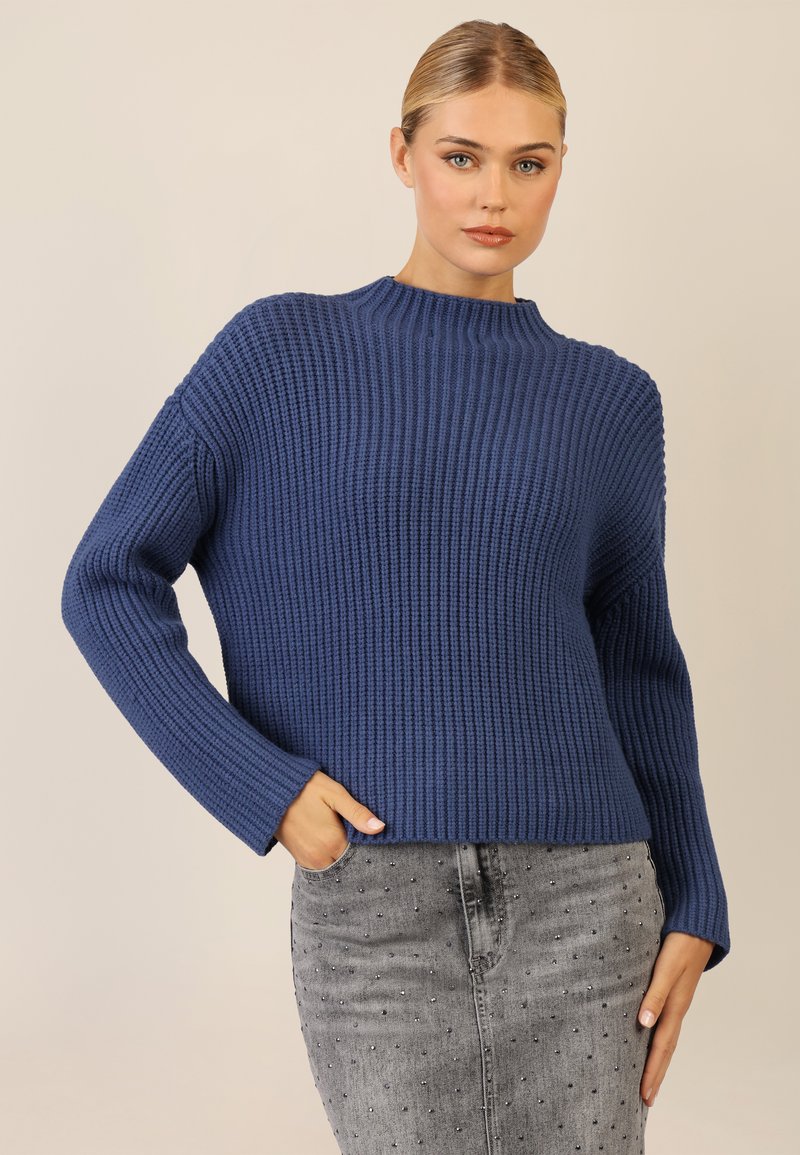 Granatowy sweter z prążkowanej dzianiny o wysokim kołnierzu i długich rękawach, zestawiony z szarym dżinsowym spódnicą z ozdobnymi detalami.