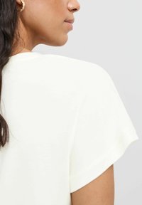 Ljusgul t-shirt i mjukt tyg, med korta ärmar och avslappnad passform. Sömdetalj längs halsringningen och axeln.
