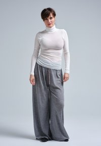 Lett, langærmet hvid kravetrøje kombineret med løse, grå drawstring-bukser. Tøjet har en blød tekstur og en afslappet pasform.
