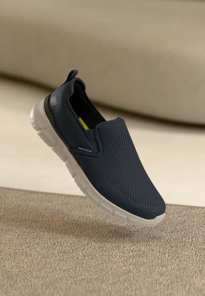 Zapato azul marino sin cordones, hecho de malla transpirable con una suela blanca ligera. Presenta una parte superior texturizada y una lengüeta en el talón para facilitar el uso.