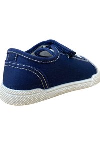 Zapato de lona azul marino con costuras blancas, puntera redondeada y correa de Velcro. La suela de goma presenta un agarre texturizado y una marca en el lateral.