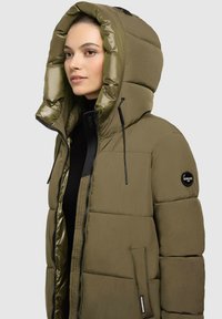 Olijfgroene pufferjack met een grote capuchon kraag, geborduurde textuur, zwarte hardware en een zijzak met rits met logodetail.