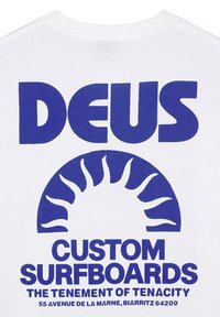 Camiseta blanca con texto azul bold: "DEUS CUSTOM SURFBOARDS" y gráfico de un sol con rayos estilizados en el centro.