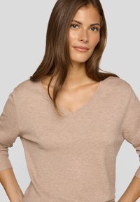 Hellbrauner V-Ausschnitt-Pullover aus weichem Material, mit langen Ärmeln und entspannter Passform, mit glatter Textur und dezenten Nahtdetails.