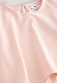 Jasnoróżowy top o miękkiej, gładkiej fakturze i okrągłym dekolcie. Posiada zapięcie na guziki z tyłu oraz luźny, zwiewny krój.
