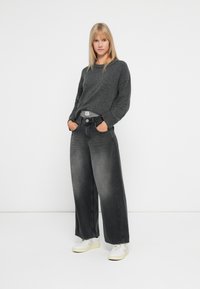 Šedý oversized svetr spárovaný s volnými vybledlými černými džíny a bílými teniskami. Tento outfit má uvolněný střih a jednoduché textury.