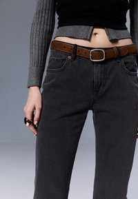 Harmaat farkut suoran lahkeen fitillä, joissa on ruskea nahkavyö ja ribattu harmaa neule. Metallinen sormus kädessä lisää yksityiskohtia.