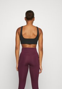 Black sports bra with a wide square back and thick straps, paired with high-waisted maroon leggings featuring a smooth texture.